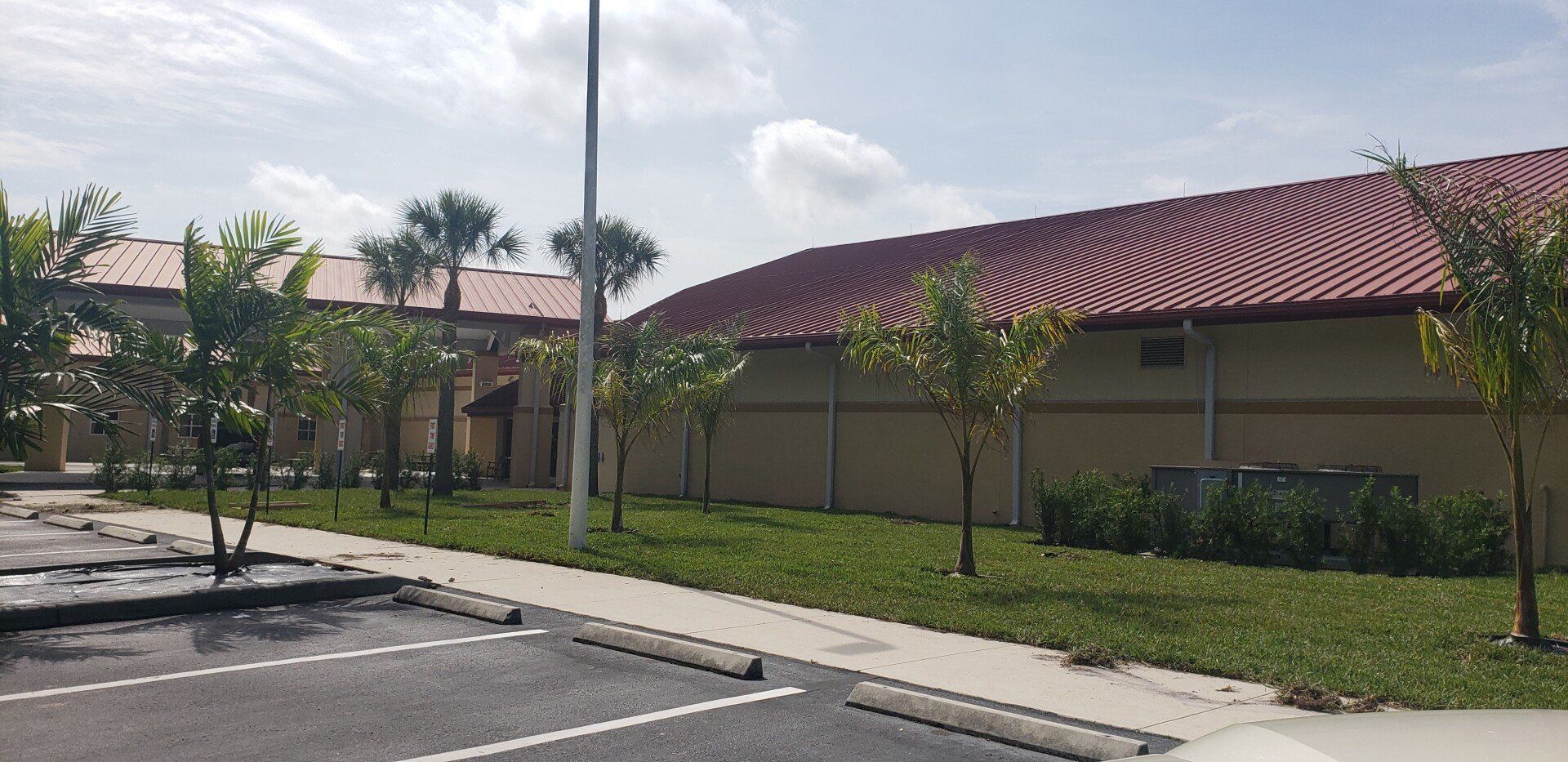 Building with red tiled roof and palm trees in front; parking lot in foreground.