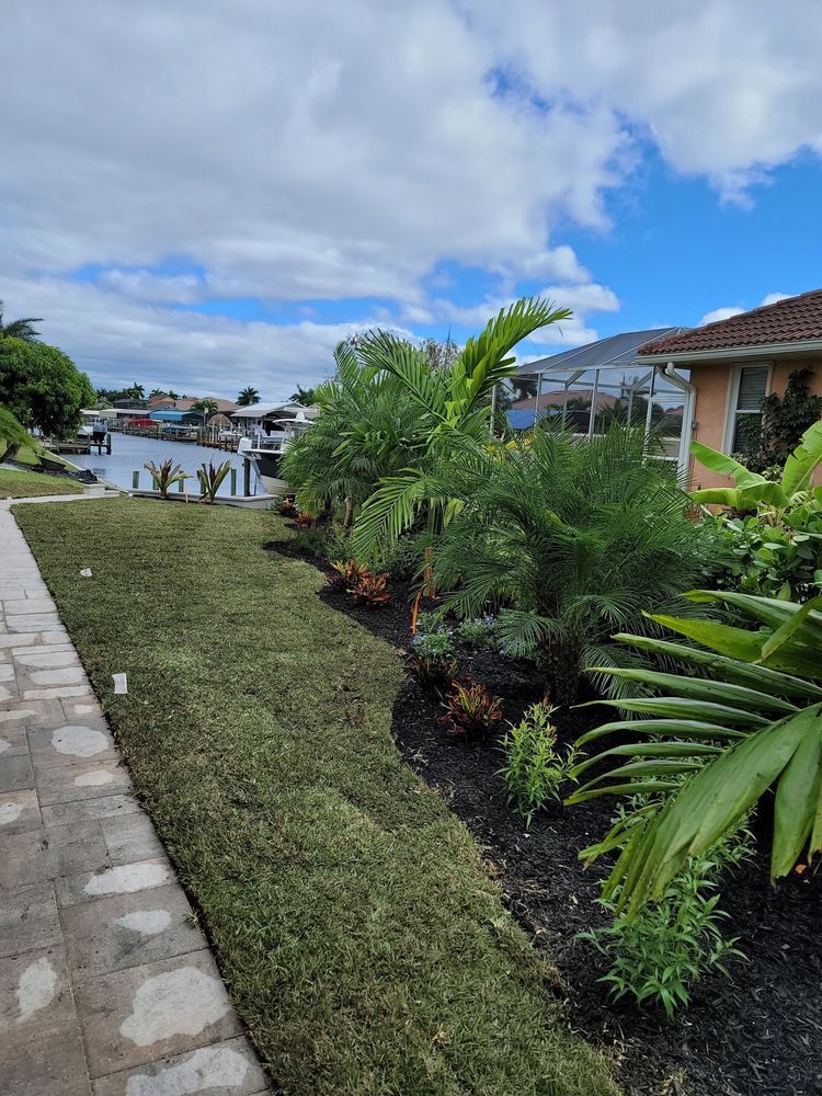 Lush green landscaping with palm trees, canal, and house under a partly cloudy sky.