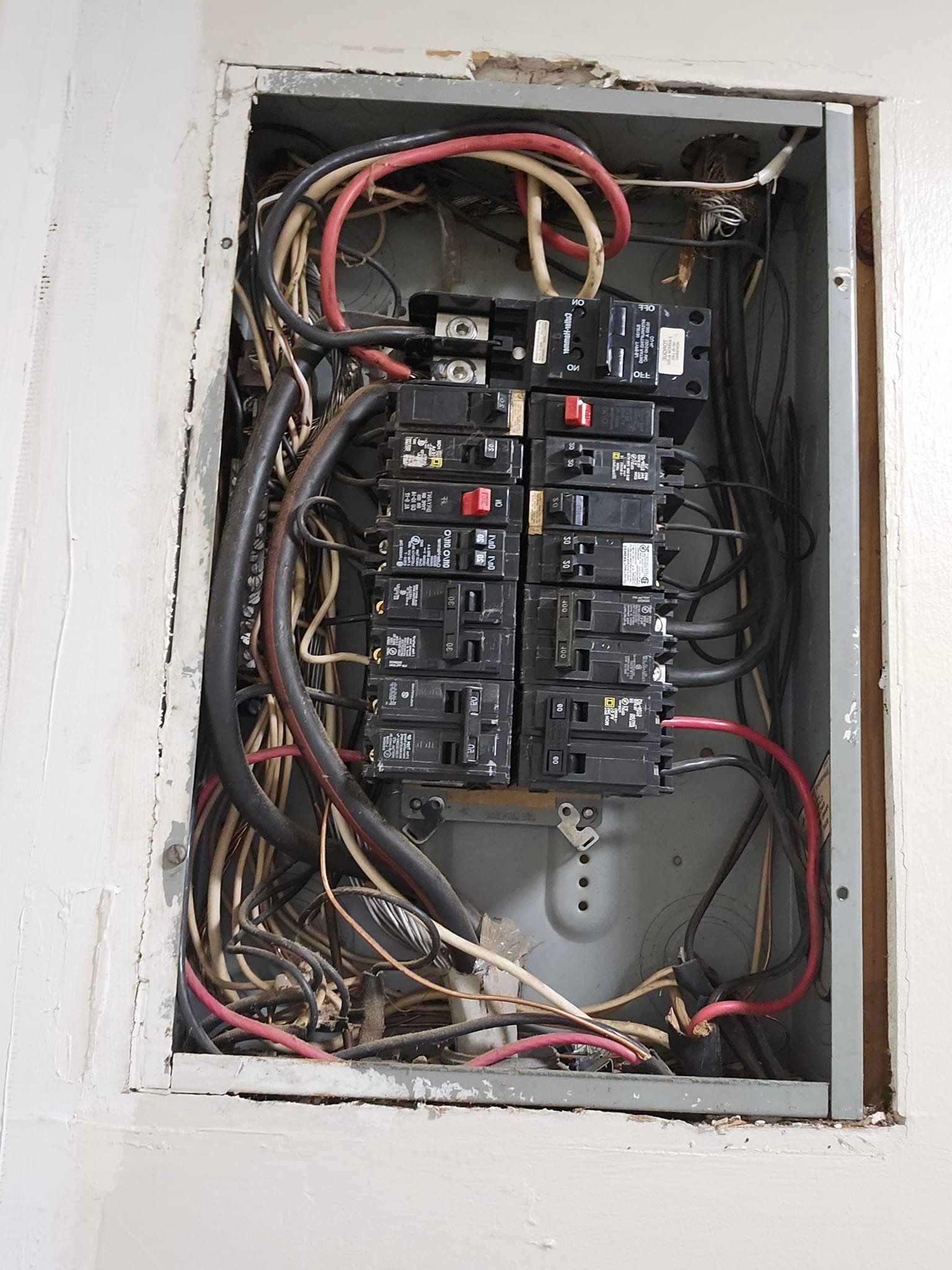 Open electrical panel with numerous black circuit breakers and wires.