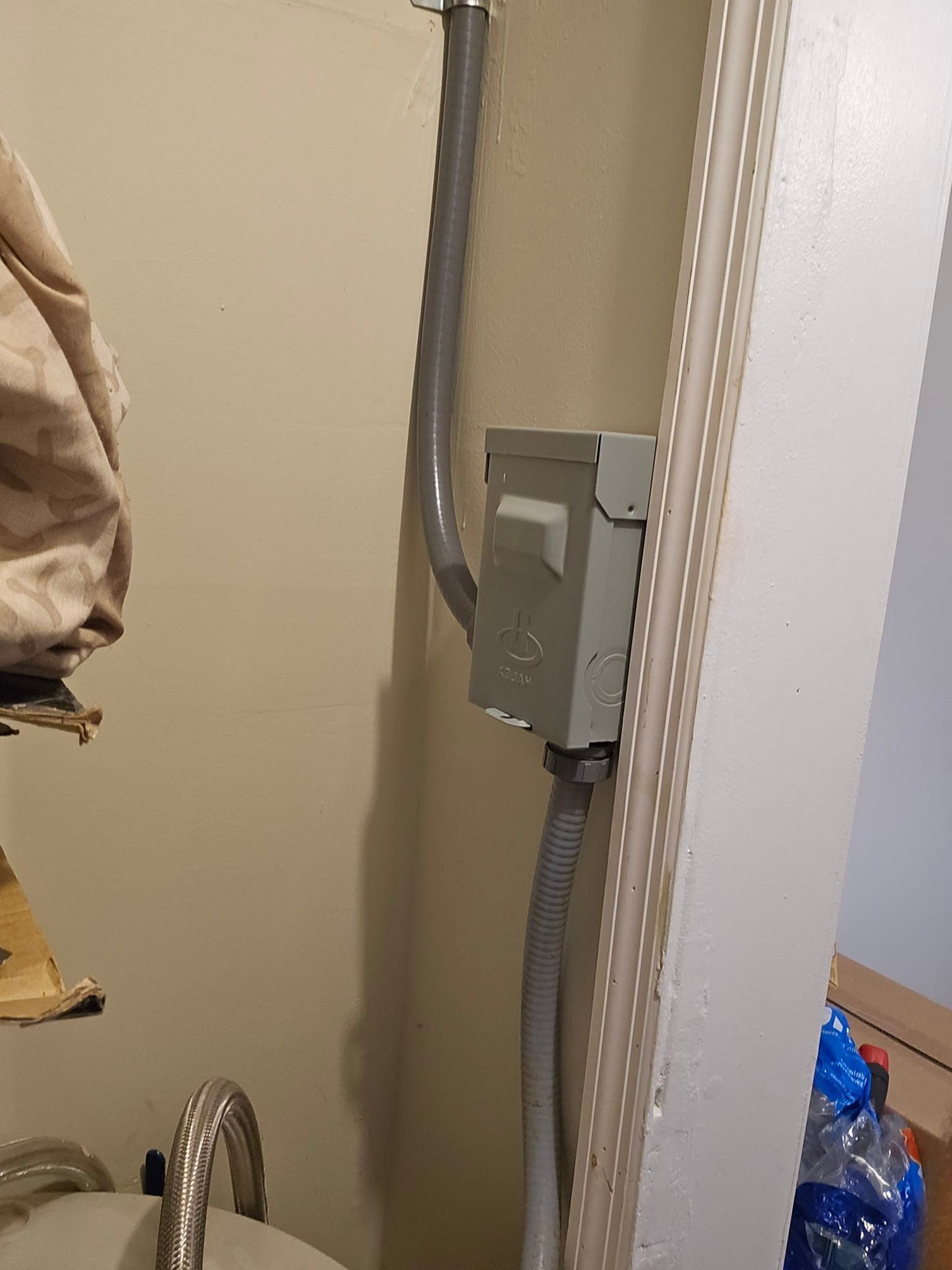 Electrical box on a beige wall, with conduit running upward. A white trim piece is to the right.