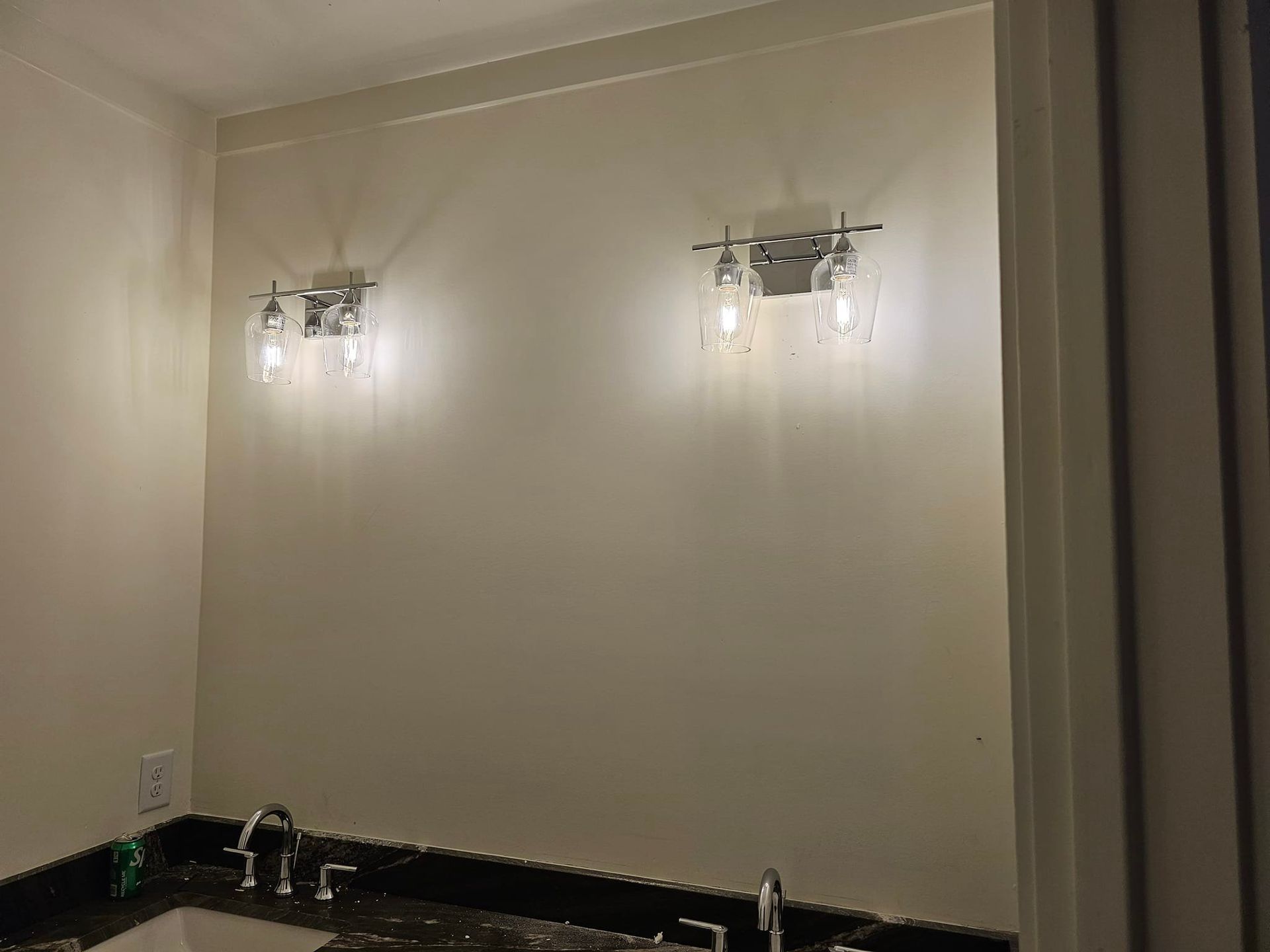 Two chrome sconce lights flank a wall above a dark countertop and sink.