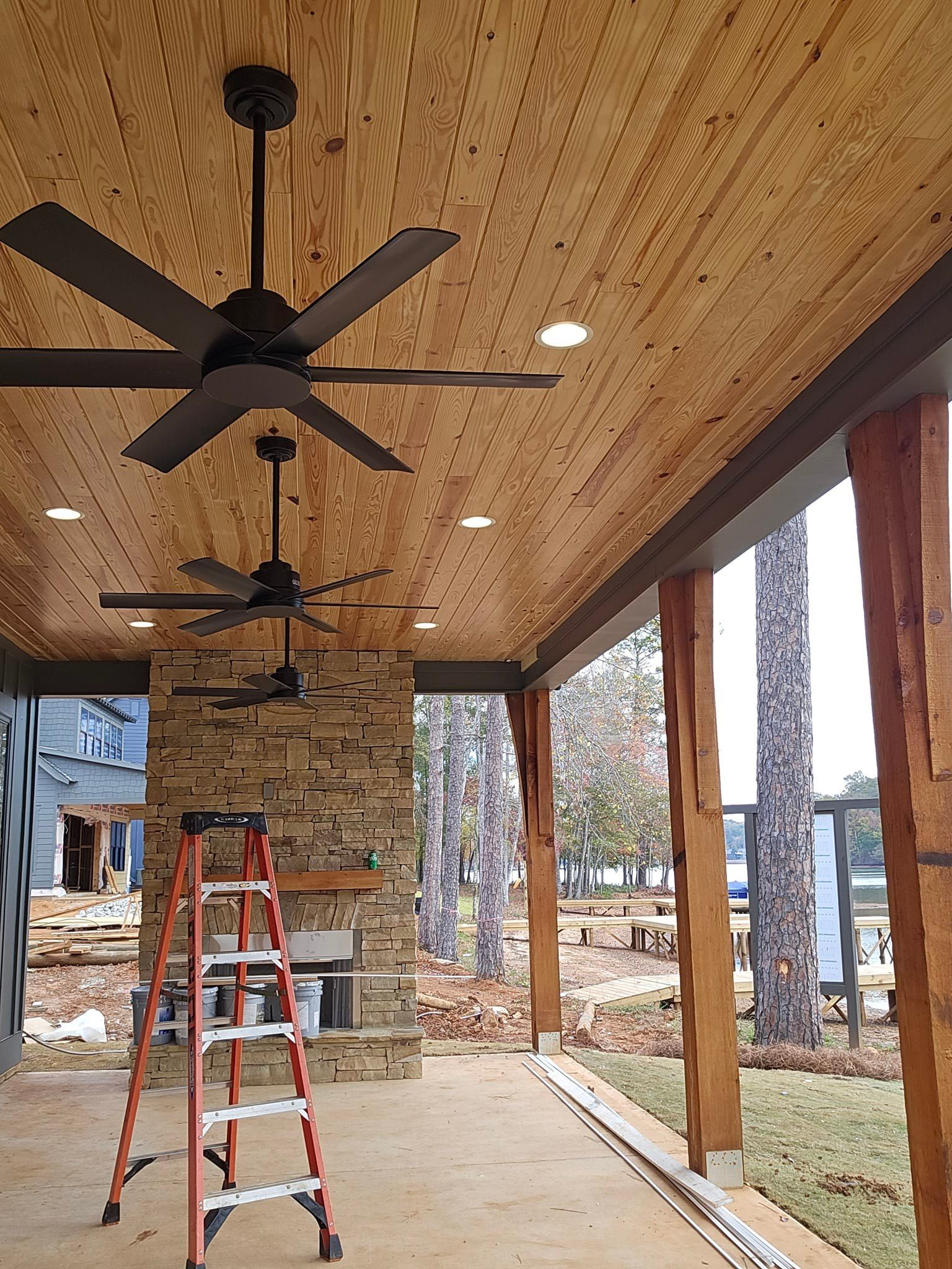 Outdoor patio under construction with ceiling fans, recessed lights, and stone fireplace.