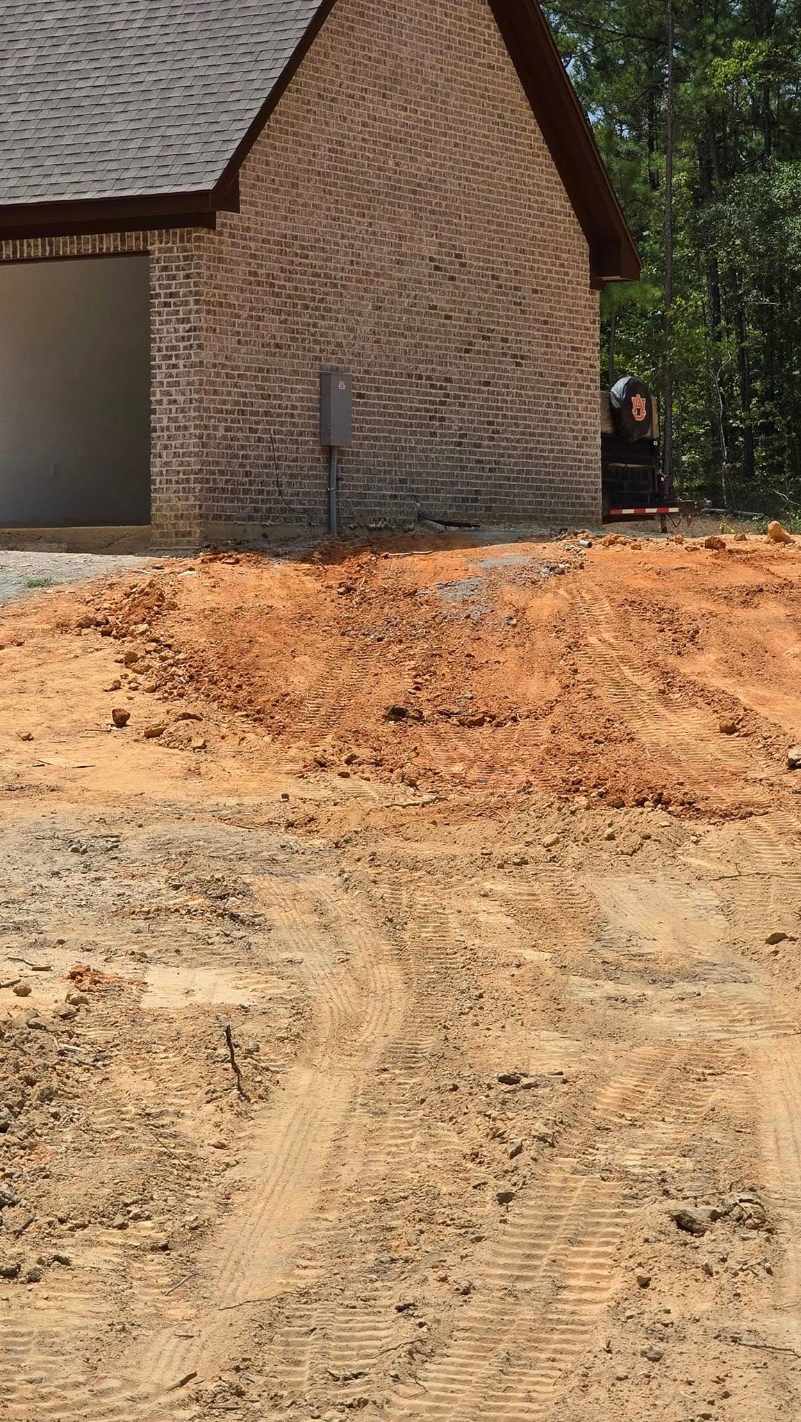 Red clay and dirt in front of a brick building under construction; trees in background.