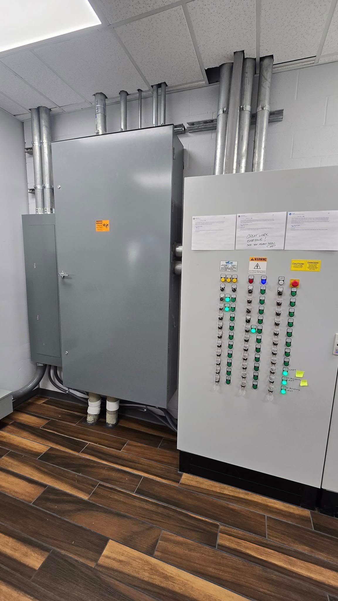 Electrical control panel and conduits mounted on a wall in a room with wood flooring.