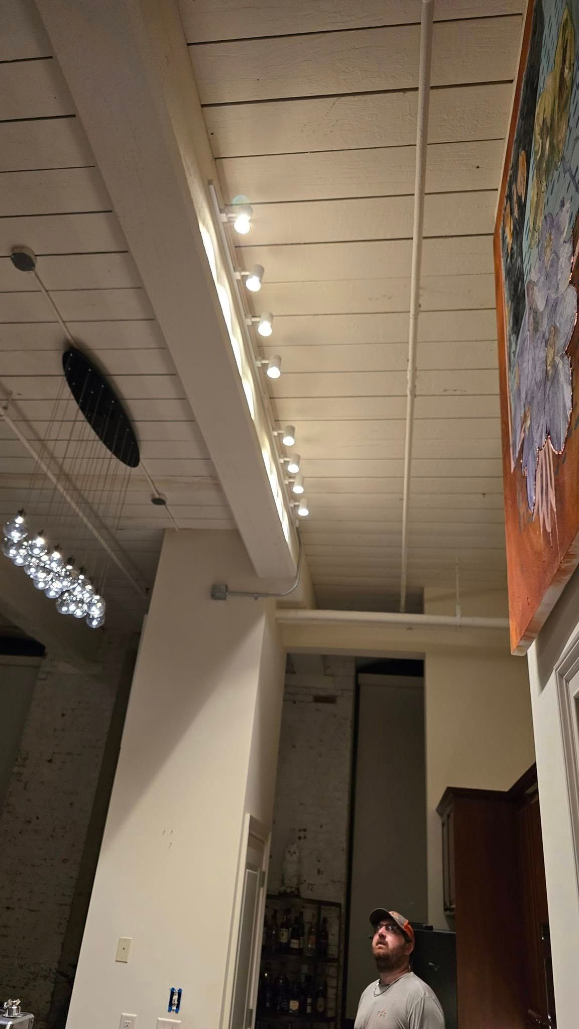 Man looking up at ceiling lights in a room with white walls and a mural.