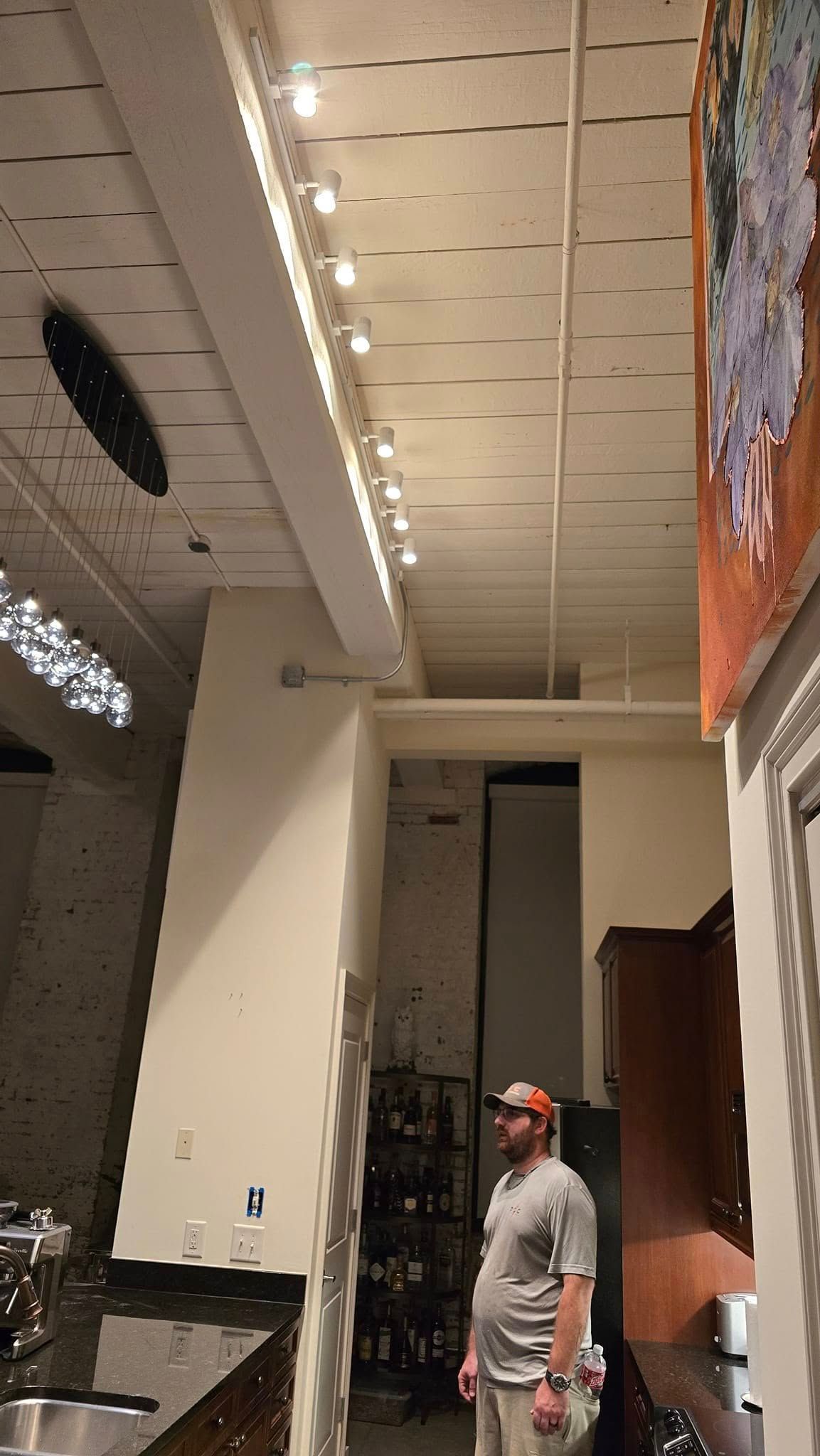 Man looking up in a commercial interior; recessed ceiling lights, artwork, and cabinets are visible.