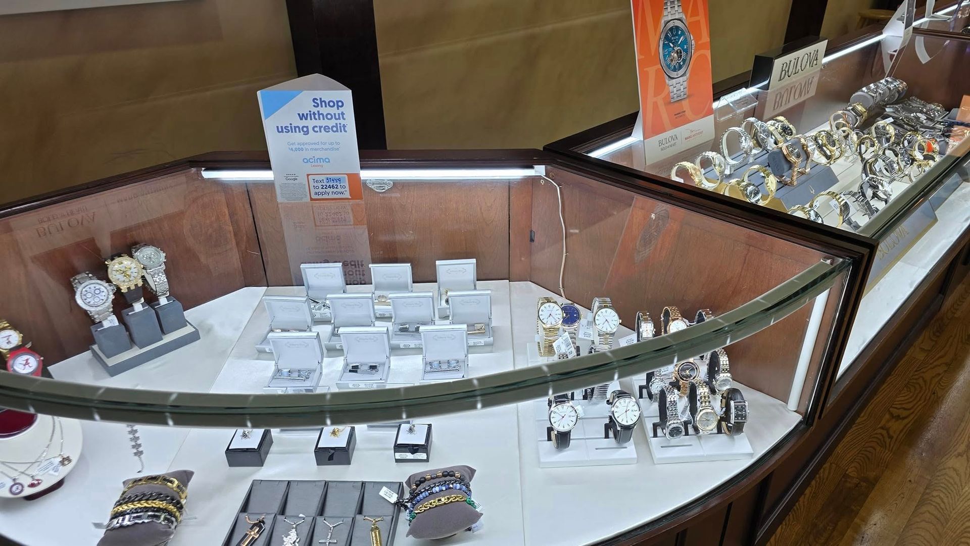 Display case with watches and jewelry in a store. Brown wood and glass. Bright lighting.
