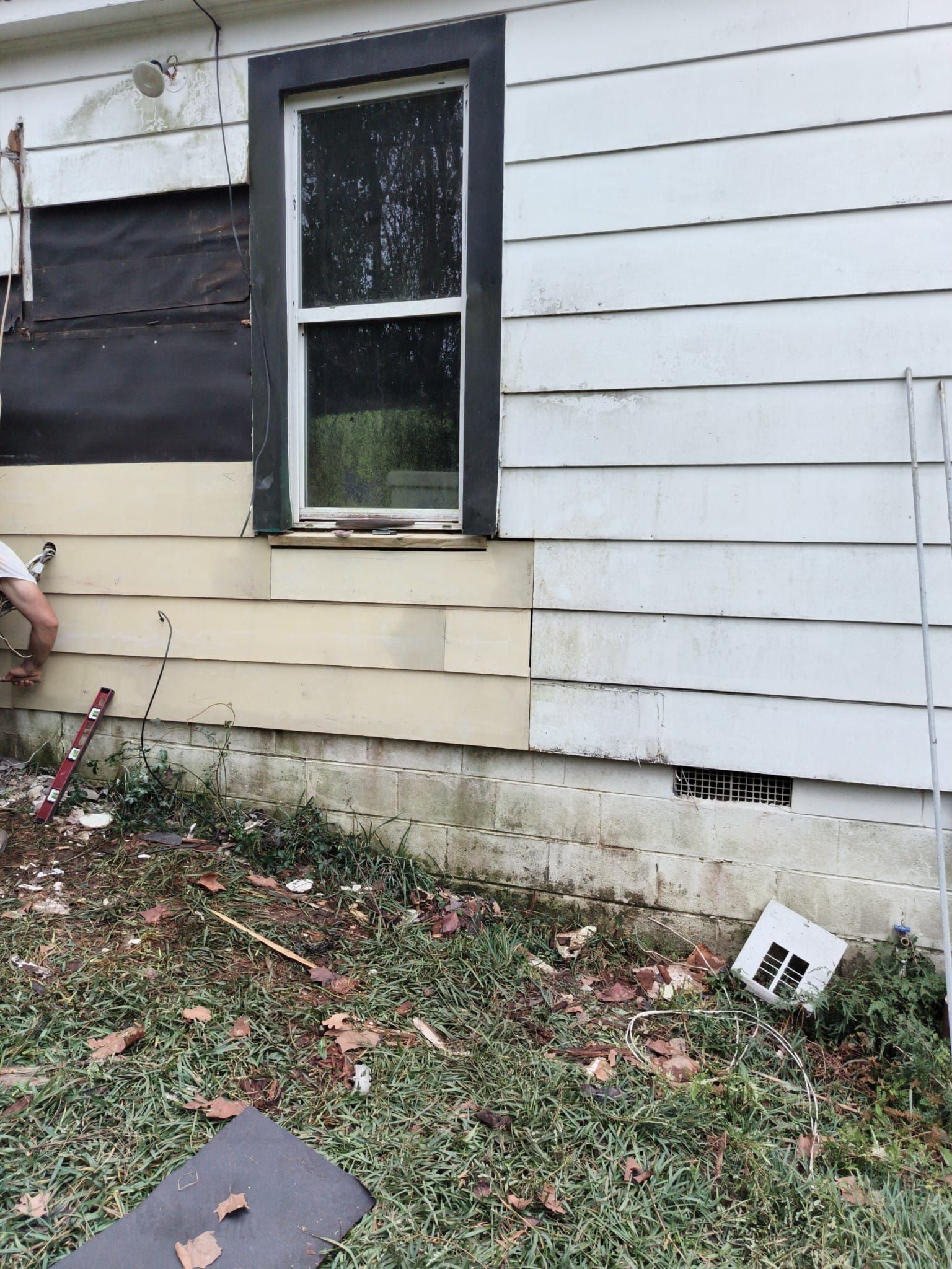 Exterior of a house with damaged siding and a window being worked on, with exposed black material.