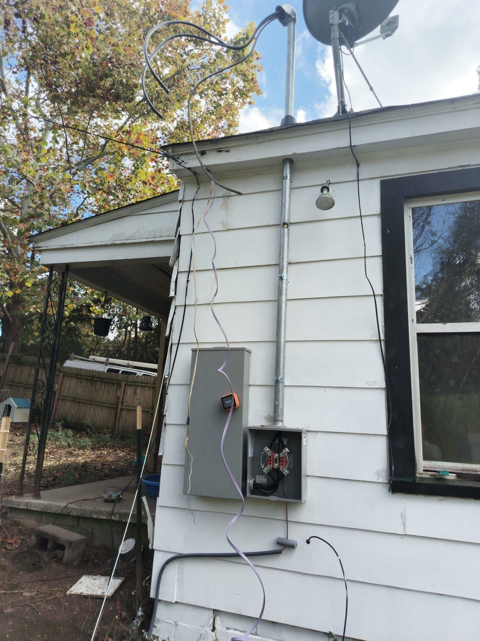Exterior electrical panel mounted on a white house. Conduit and wiring are visible.