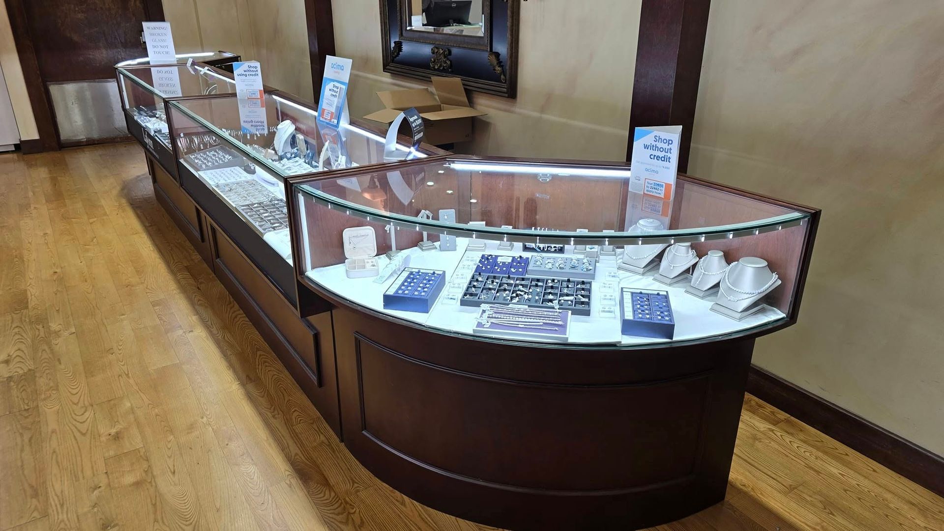 Jewelry display case in a store, wooden with glass top, displaying rings, necklaces, and watches.