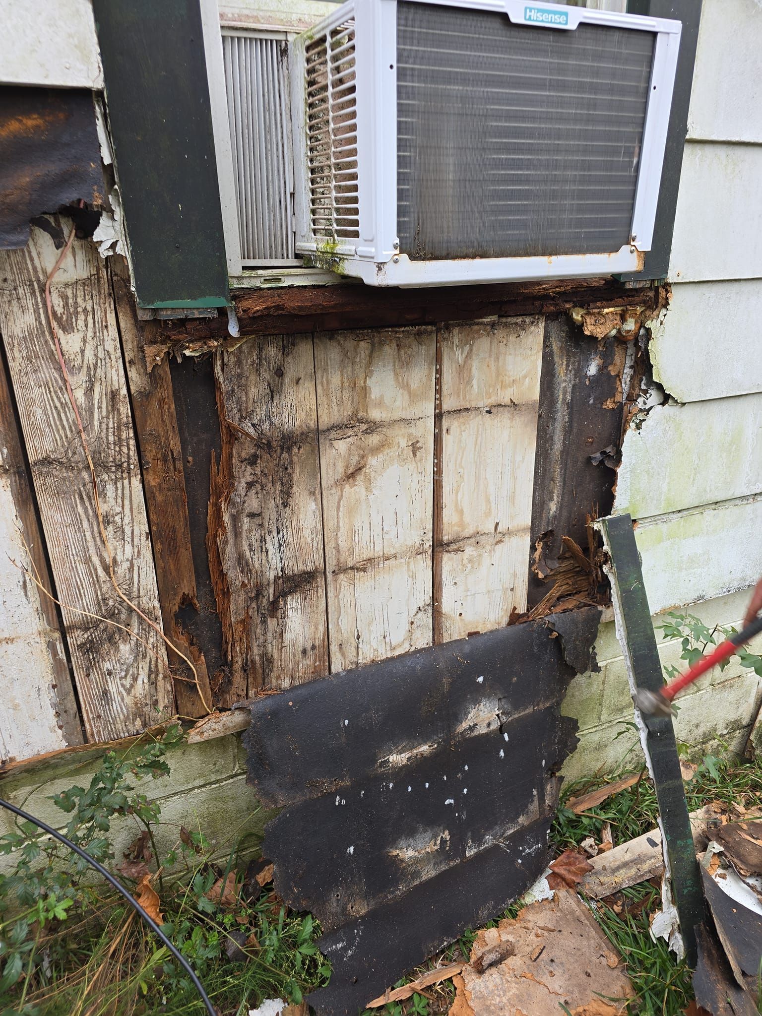 Damaged exterior wall with exposed wood and a window air conditioner.