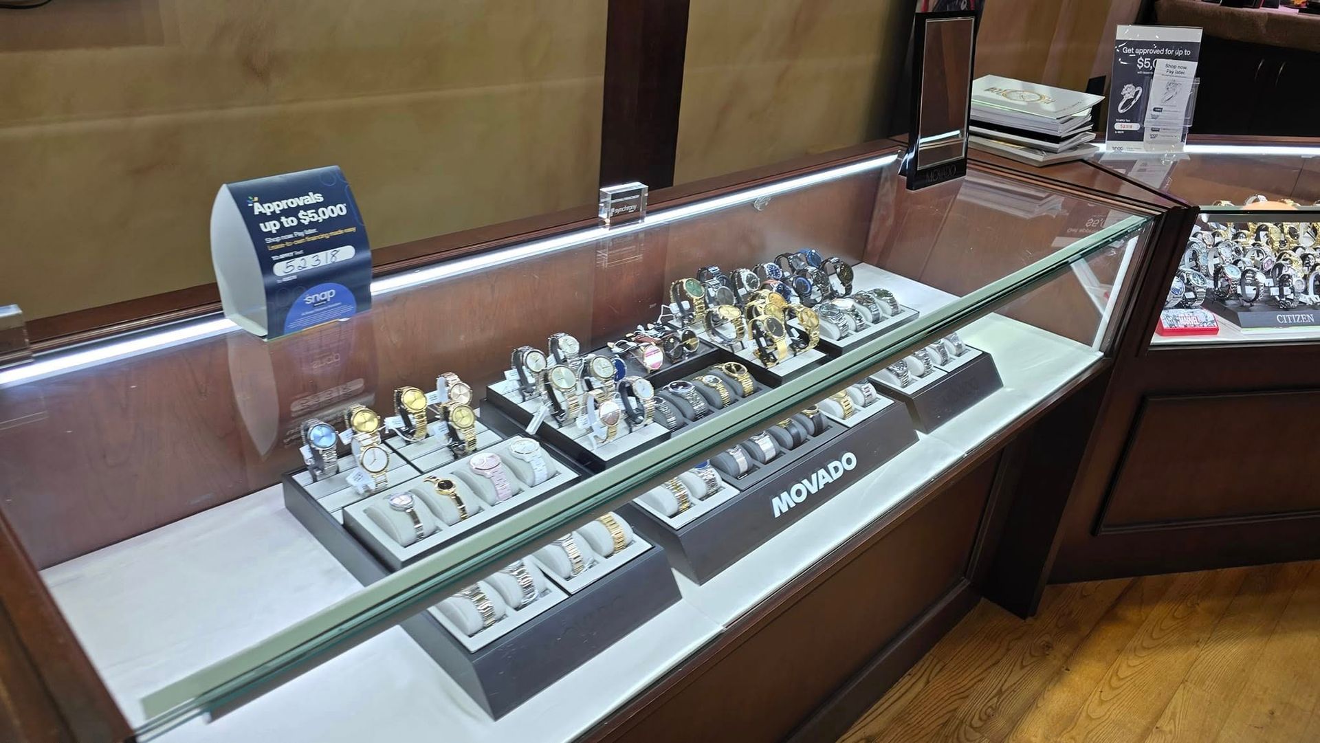 Watch display case in a store, filled with watches. Lit showcase with wooden trim and various watch styles on display.