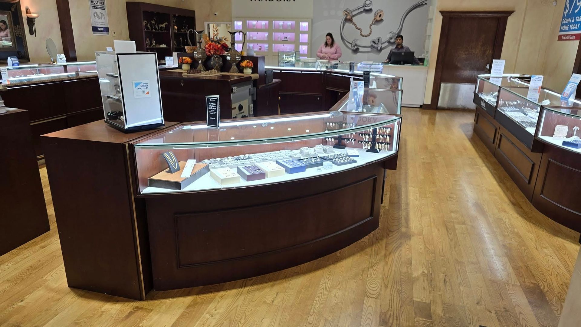 Jewelry store interior with display cases, wood flooring, and a woman in the background.