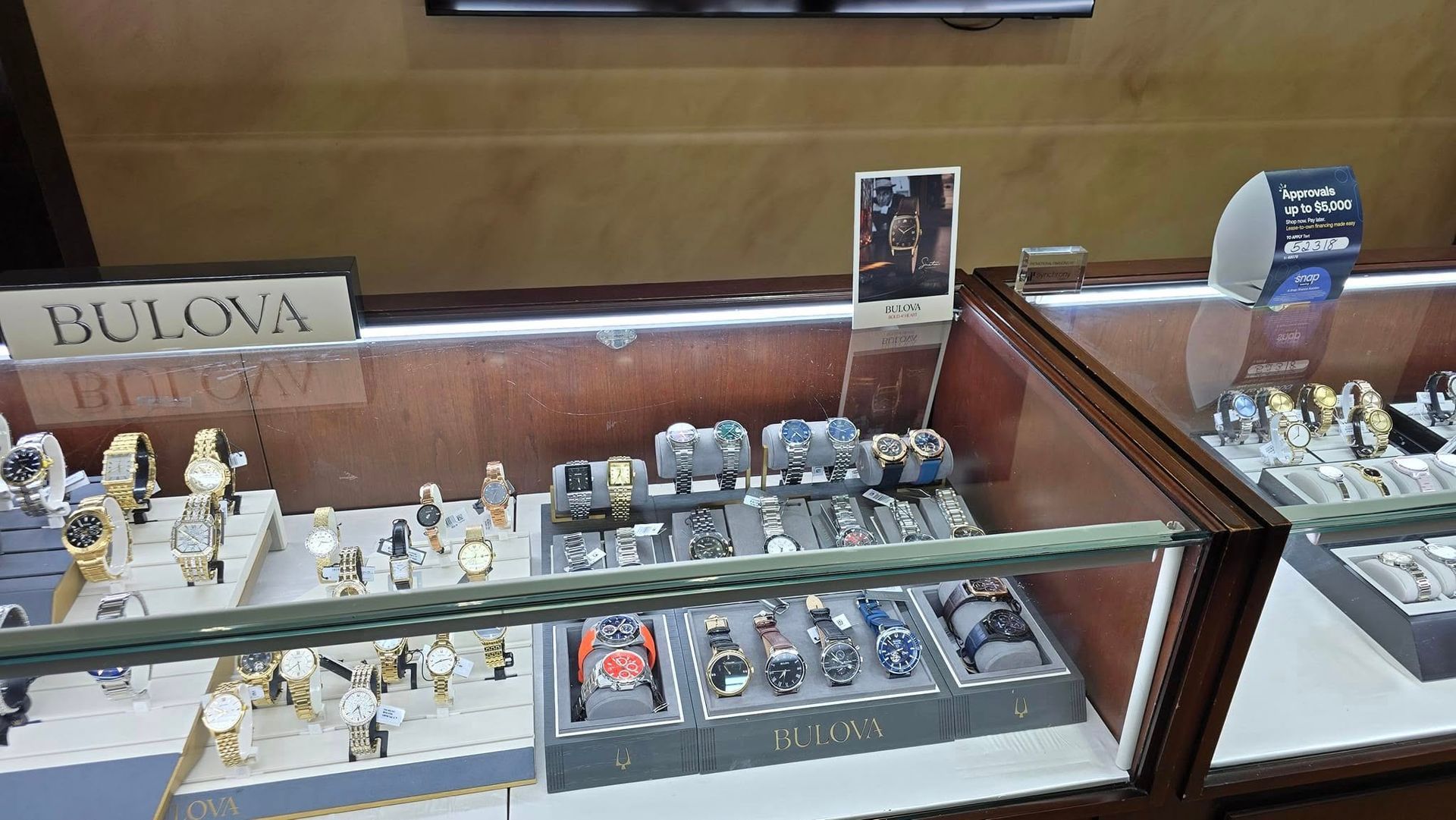 Display case of Bulova watches in a jewelry store; various styles and colors visible.