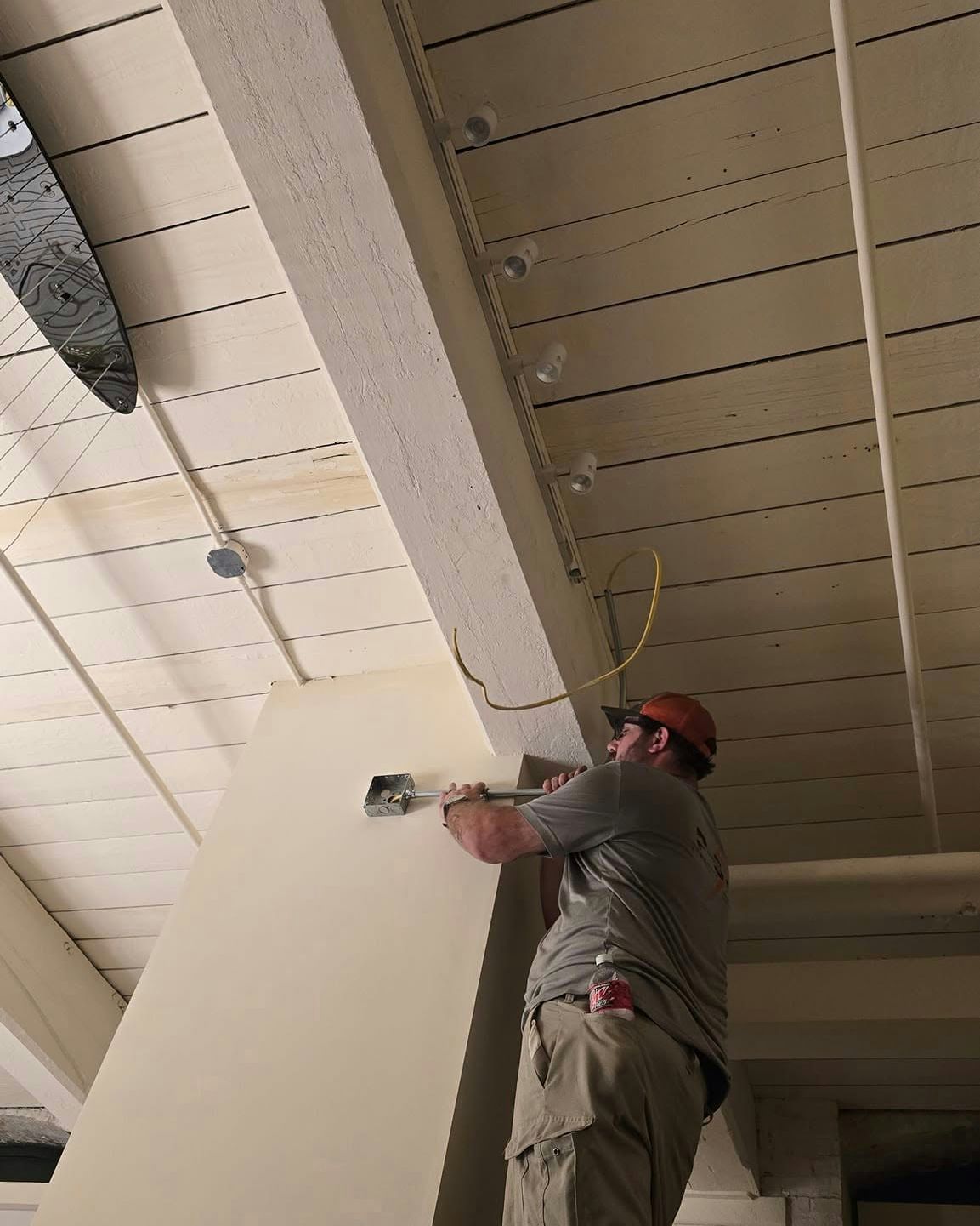 Man installing electrical box on column, beneath wood ceiling with lights.