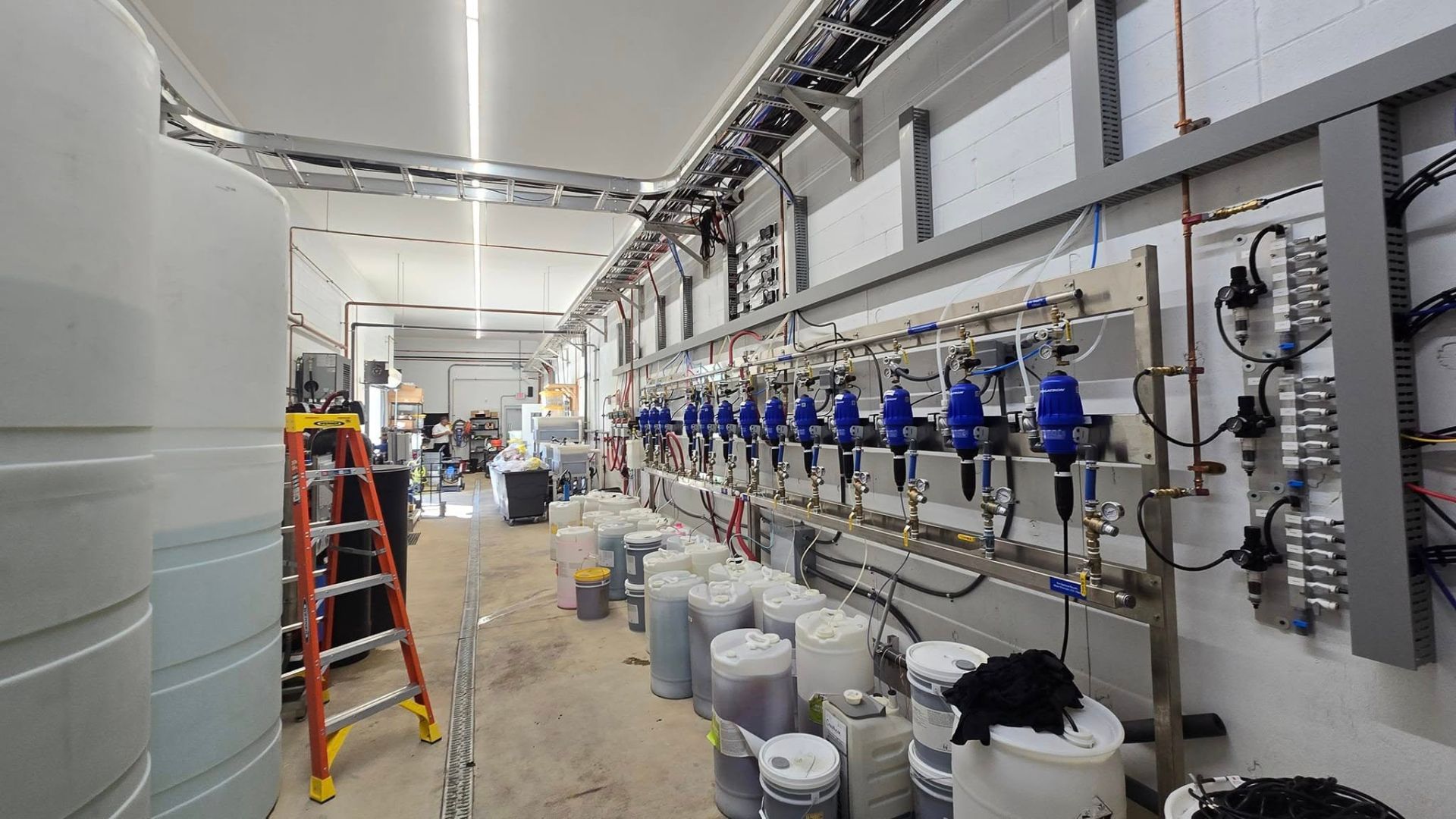 Inside a factory, rows of machinery with blue components and tanks against white walls.