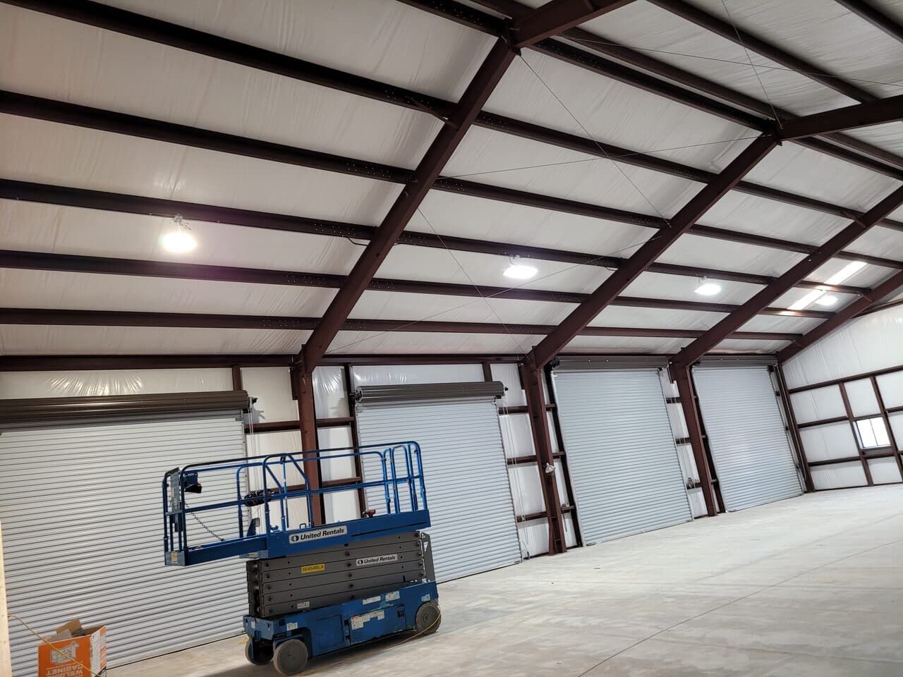 Interior view of a warehouse with roll-up doors, steel beams, and a blue lift.