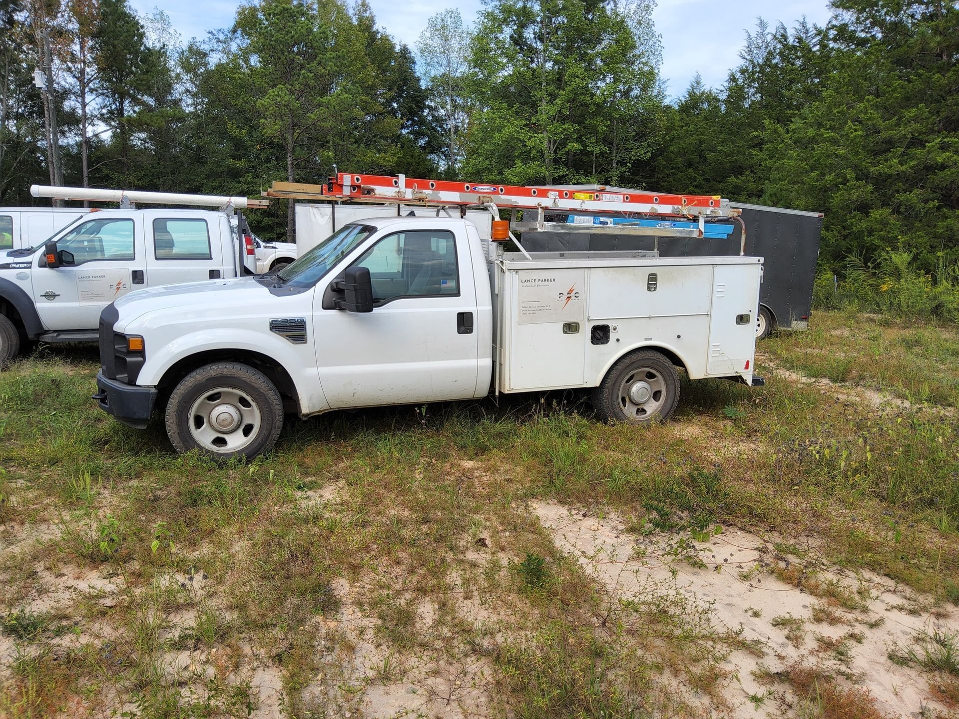White work truck parked on grassy ground, with trees in the background.