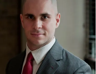 Man in grey suit and red tie, smiling slightly; indoor setting.