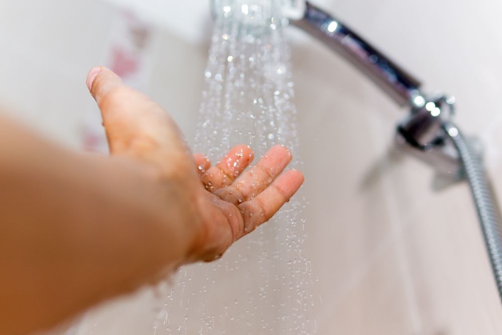 A Person Is Taking A Shower With Their Hand In The Water — Cairns Clear Water Company In Tablelands, QLD