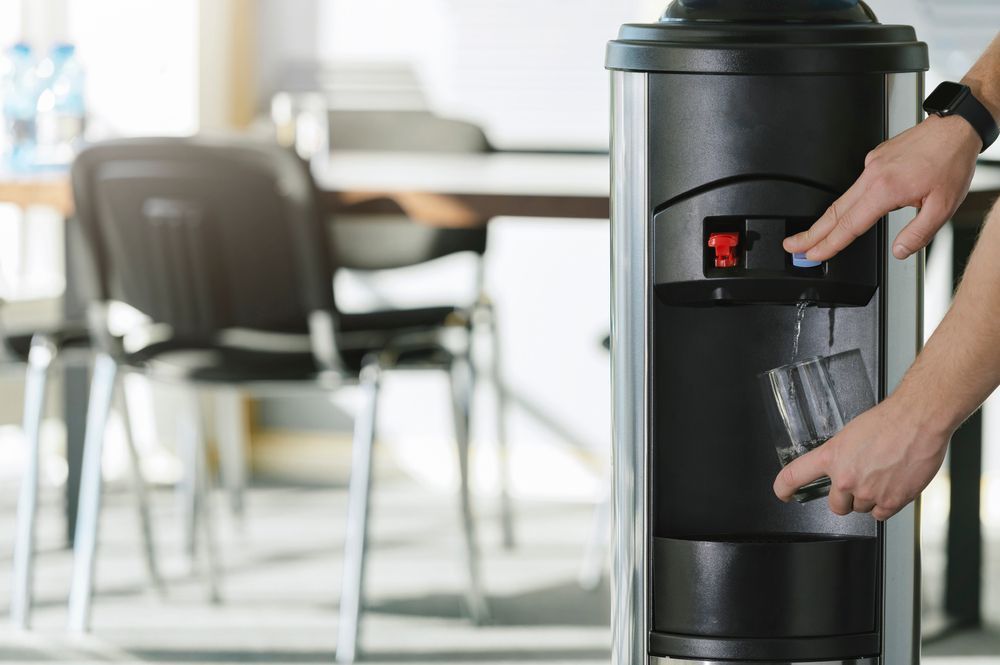 A person is pouring water into a glass from a water dispenser — Cairns Clear Water Company In Douglas Shire, QLD