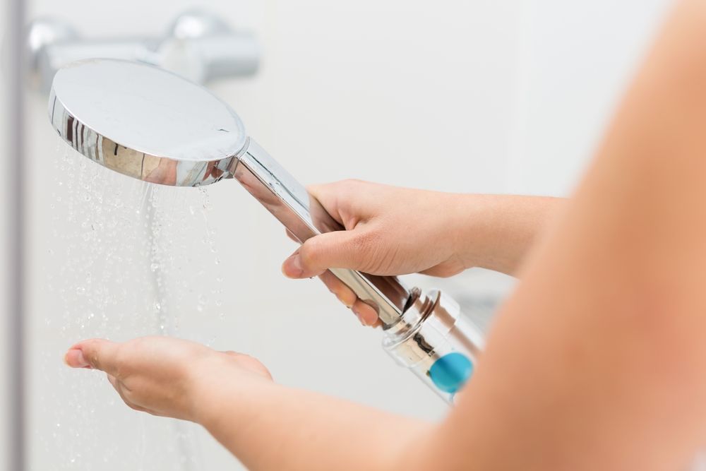 A Woman Is Holding A Shower Head In Her Hand While Taking A Shower — Cairns Clear Water Company In Cairns, QLD