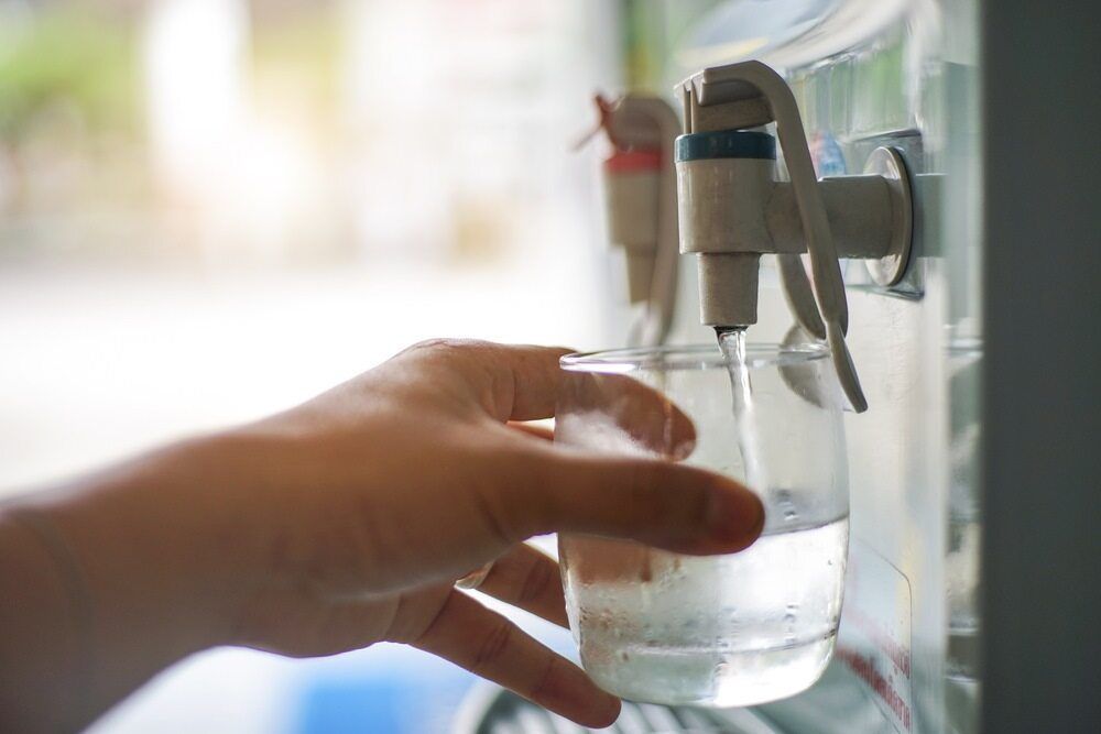 A Person Is Pouring Water Into A Glass From A Water Dispenser — Cairns Clear Water Company In Westcourt, QLD