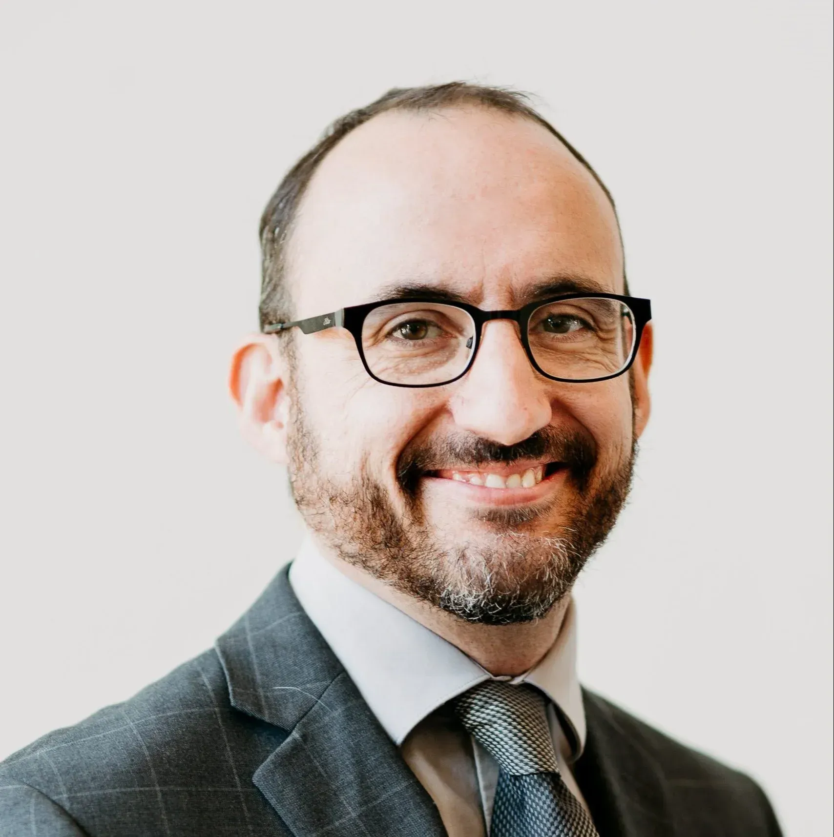 A man with glasses and a beard is wearing a suit and tie