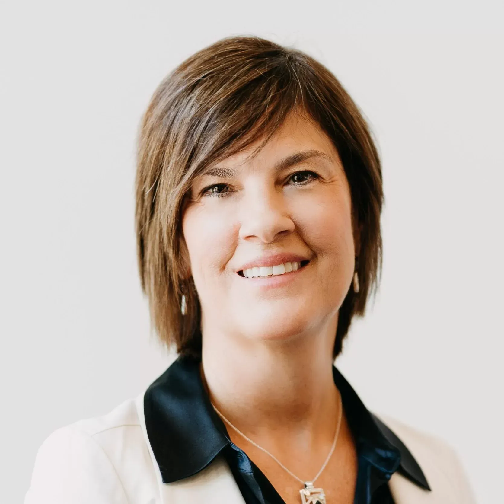 A woman wearing a black shirt and a white jacket is smiling for the camera.