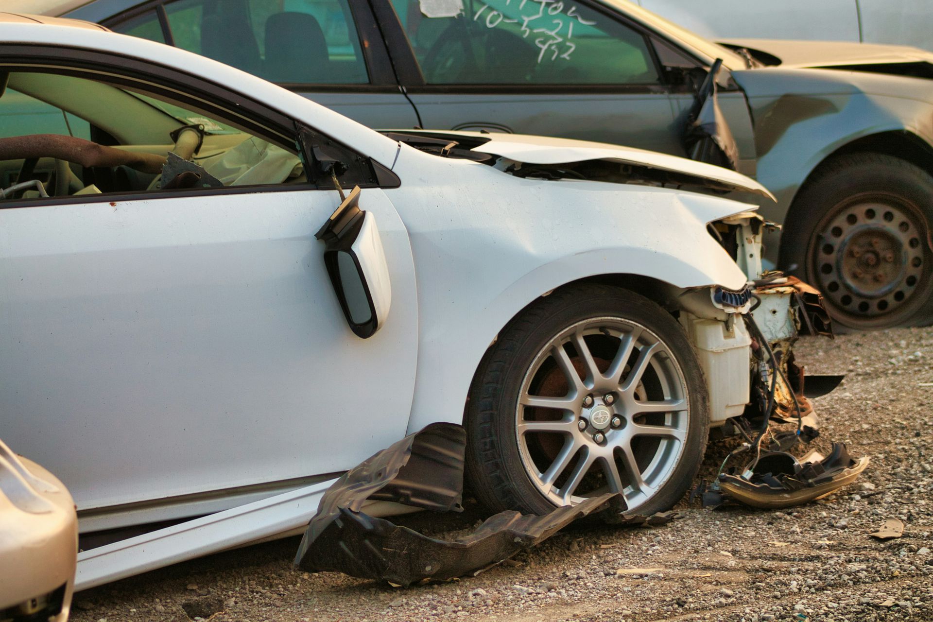 A white car is sitting in a pile of wrecked cars.