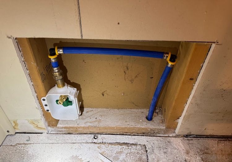 Blue and yellow PEX pipes and a valve box inside a wall opening.