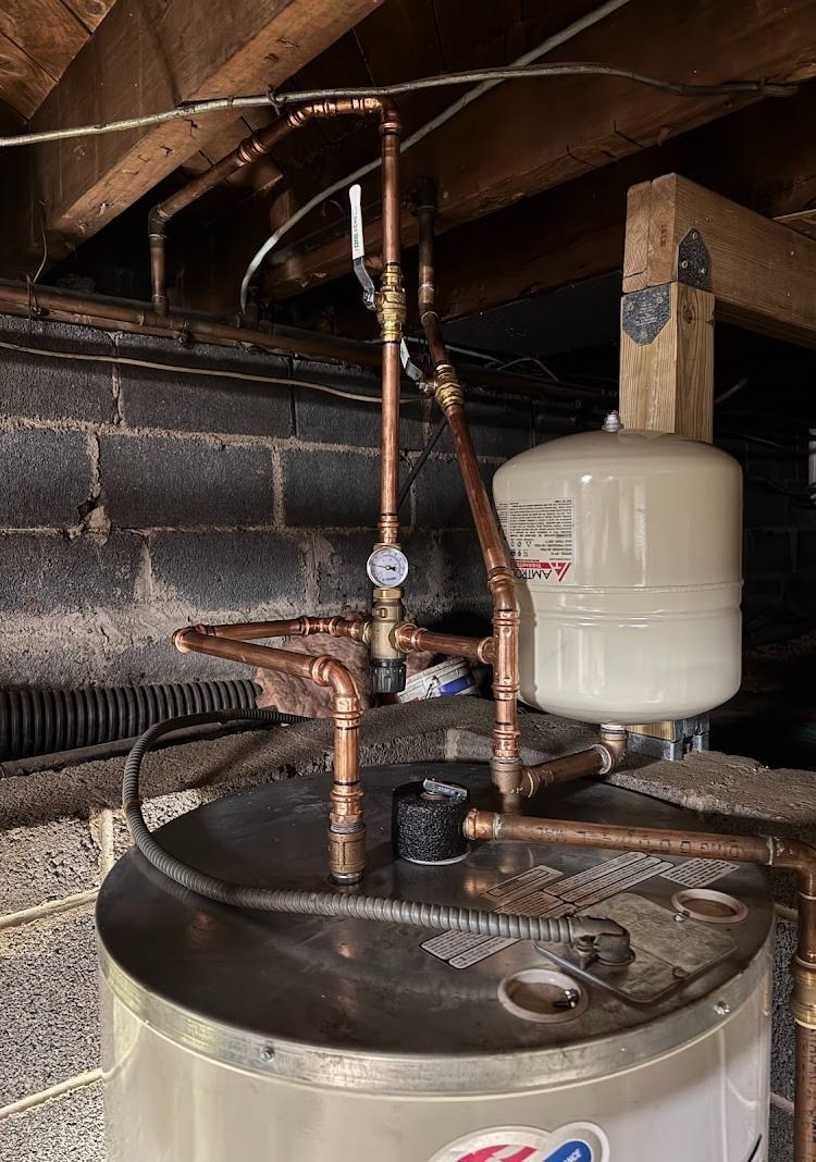 Copper pipes and valve assembly atop a hot water heater, with an expansion tank nearby.