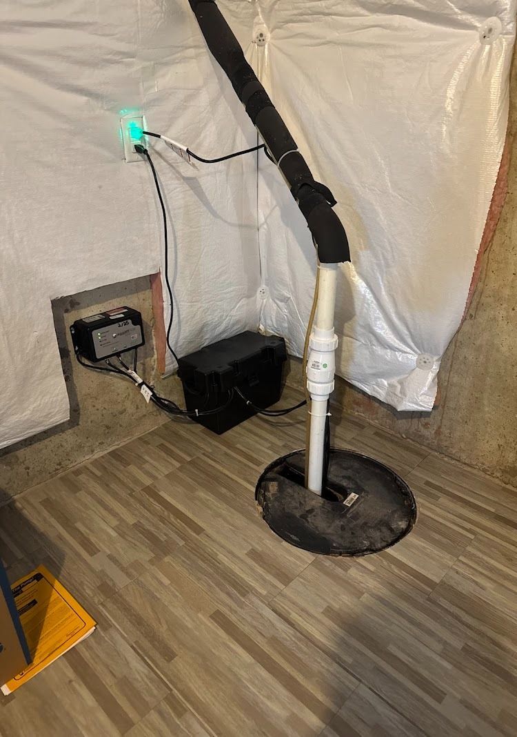 Sump pump system in a basement with a black pump, white pipe, and power cord plugged into an outlet.