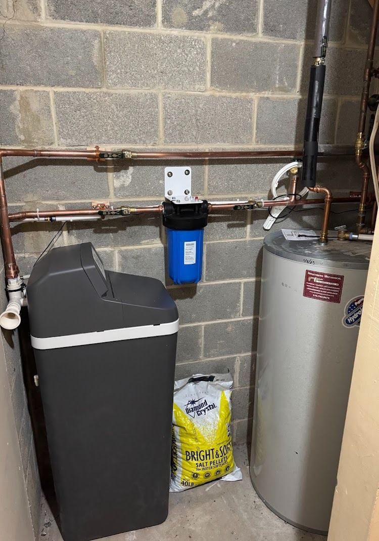 Water filtration system: A blue filter, softener, and water heater against a cinder block wall. Copper pipes.