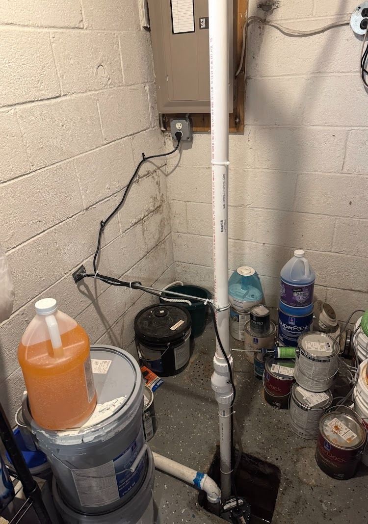 Sump pump in a basement corner, white pipe, electrical box, various containers and items.