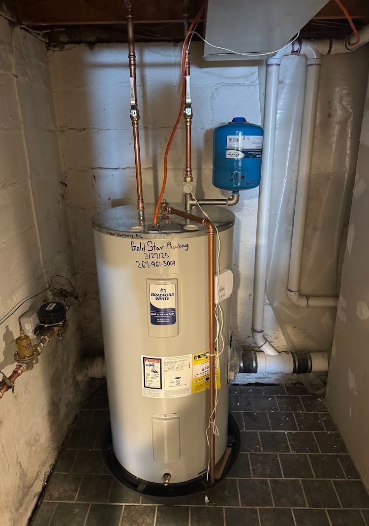 Water heater in a basement. Copper pipes connect to the tank. Blue expansion tank sits nearby.