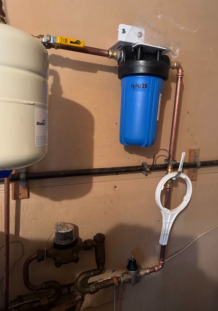 Water filtration system with blue filter, copper pipes, and a pressure tank attached to a wall.