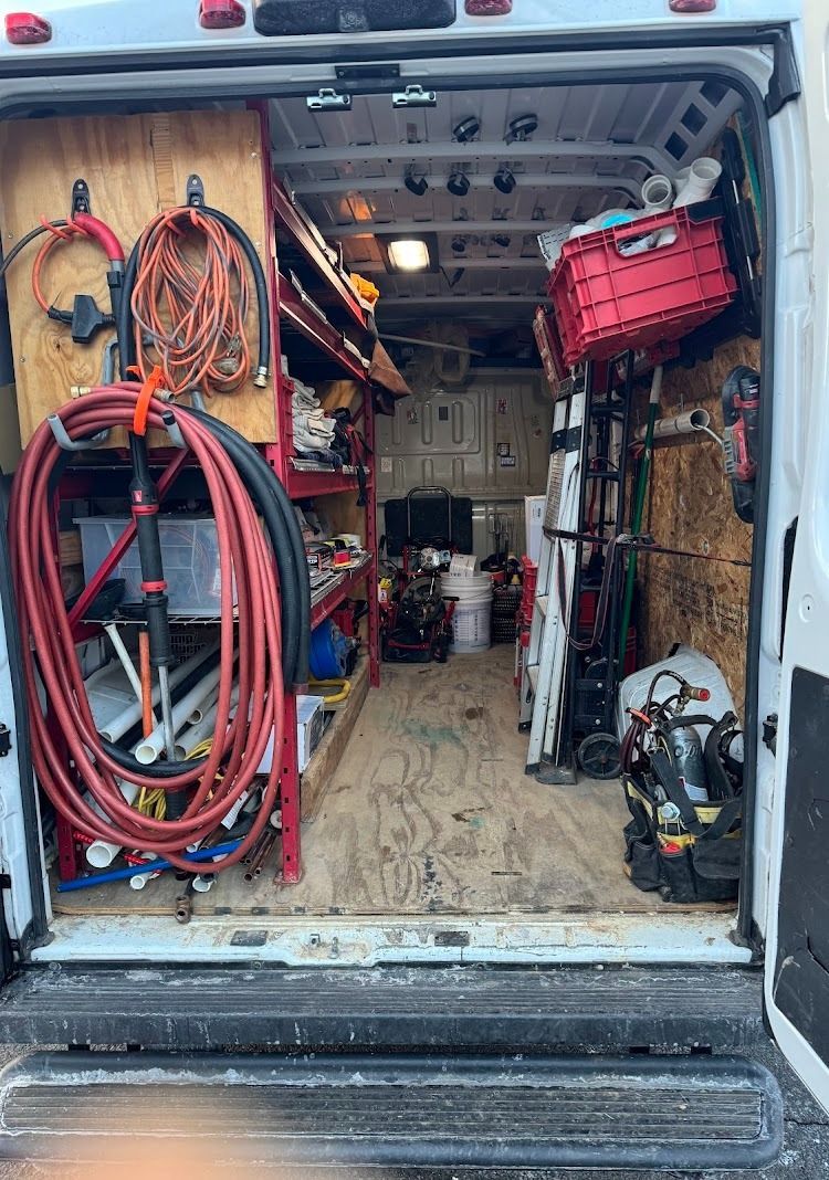 Interior of a work van, open rear doors. Shelves of tools and equipment. Red, orange, black, and silver.