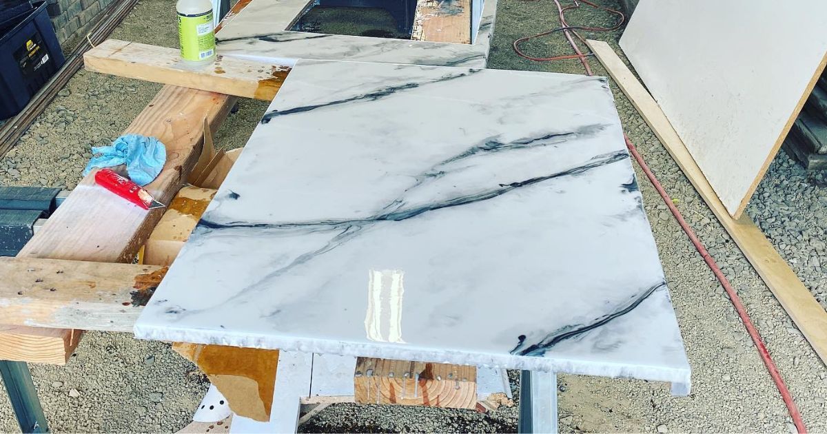 Elite Surface Coatings - White marble slab with dark gray veining, resting on a makeshift work table outside.