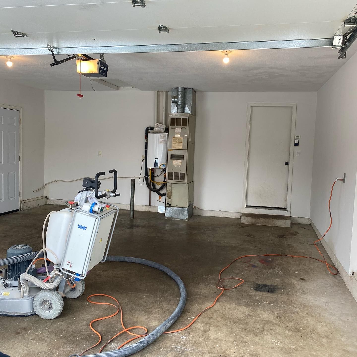 Elite Surface Coatings - Garage with concrete floor grinding machine, heating unit, and door.