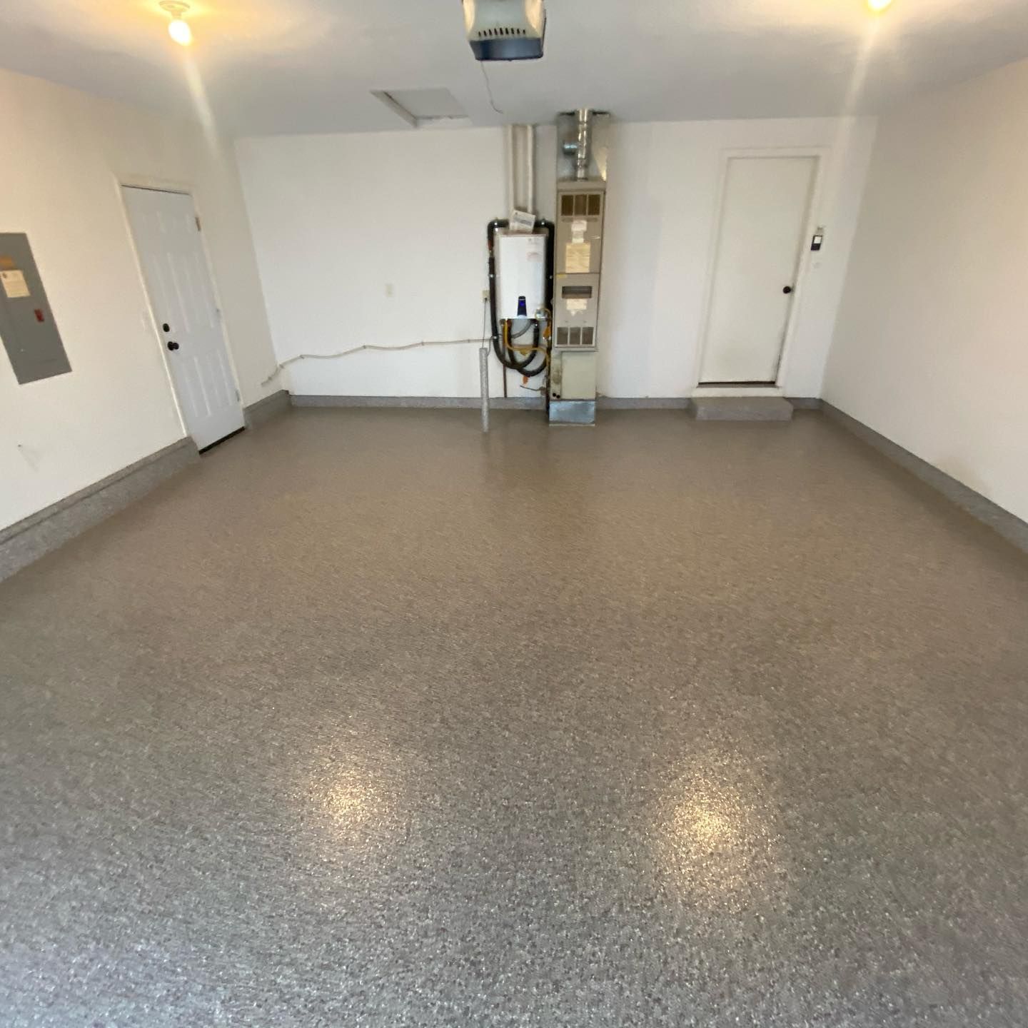 Elite Surface Coatings - Empty garage with gray speckled epoxy floor, white walls, and two doors.