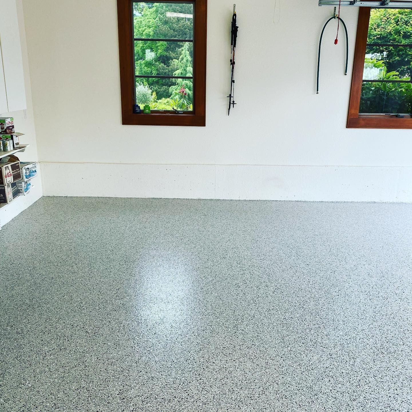 Elite Surface Coatings - Garage with speckled, gray flooring, white walls, two windows with a view, and some tools hanging.