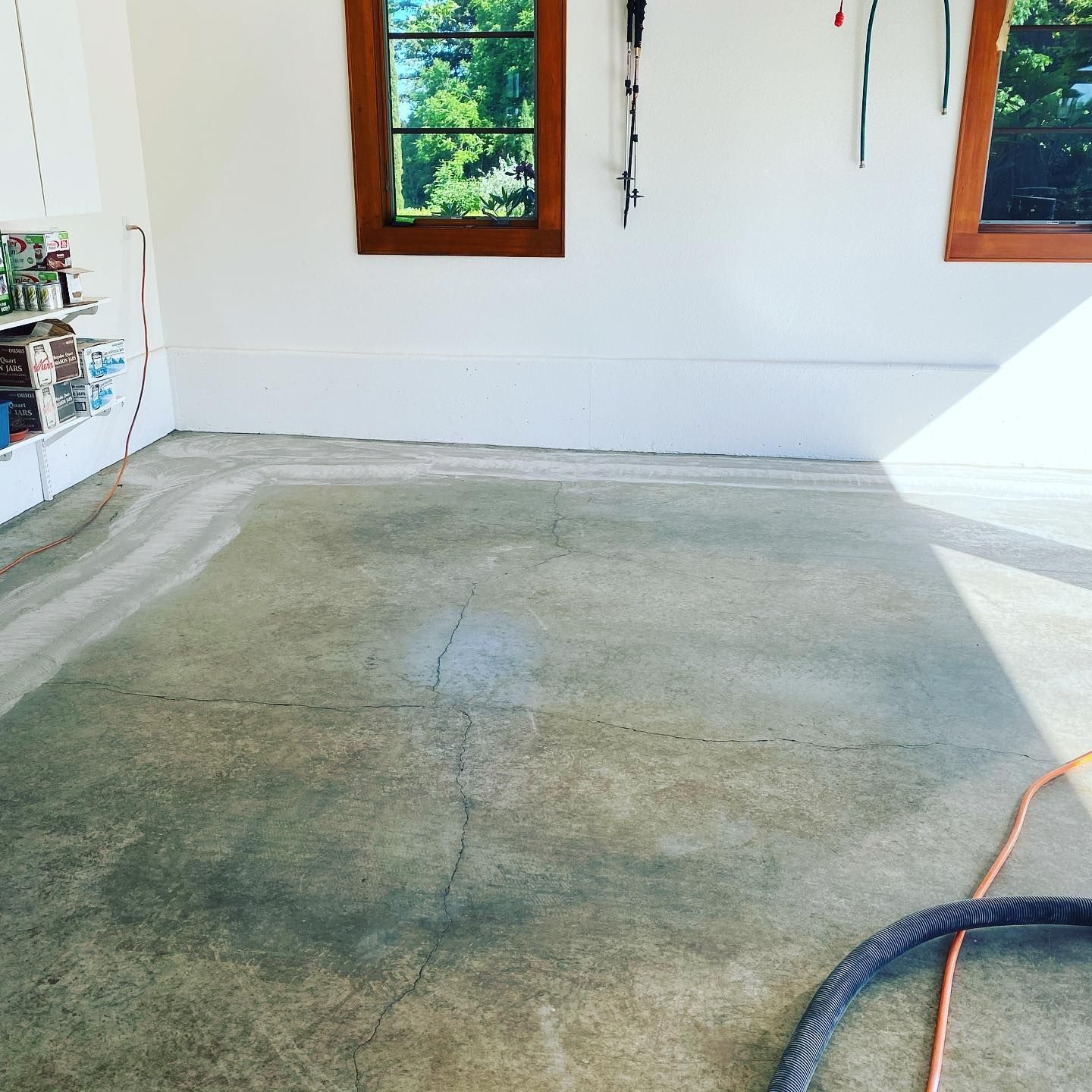 Elite Surface Coatings - Empty garage with concrete floor, white walls, wooden windows, and tools hanging.