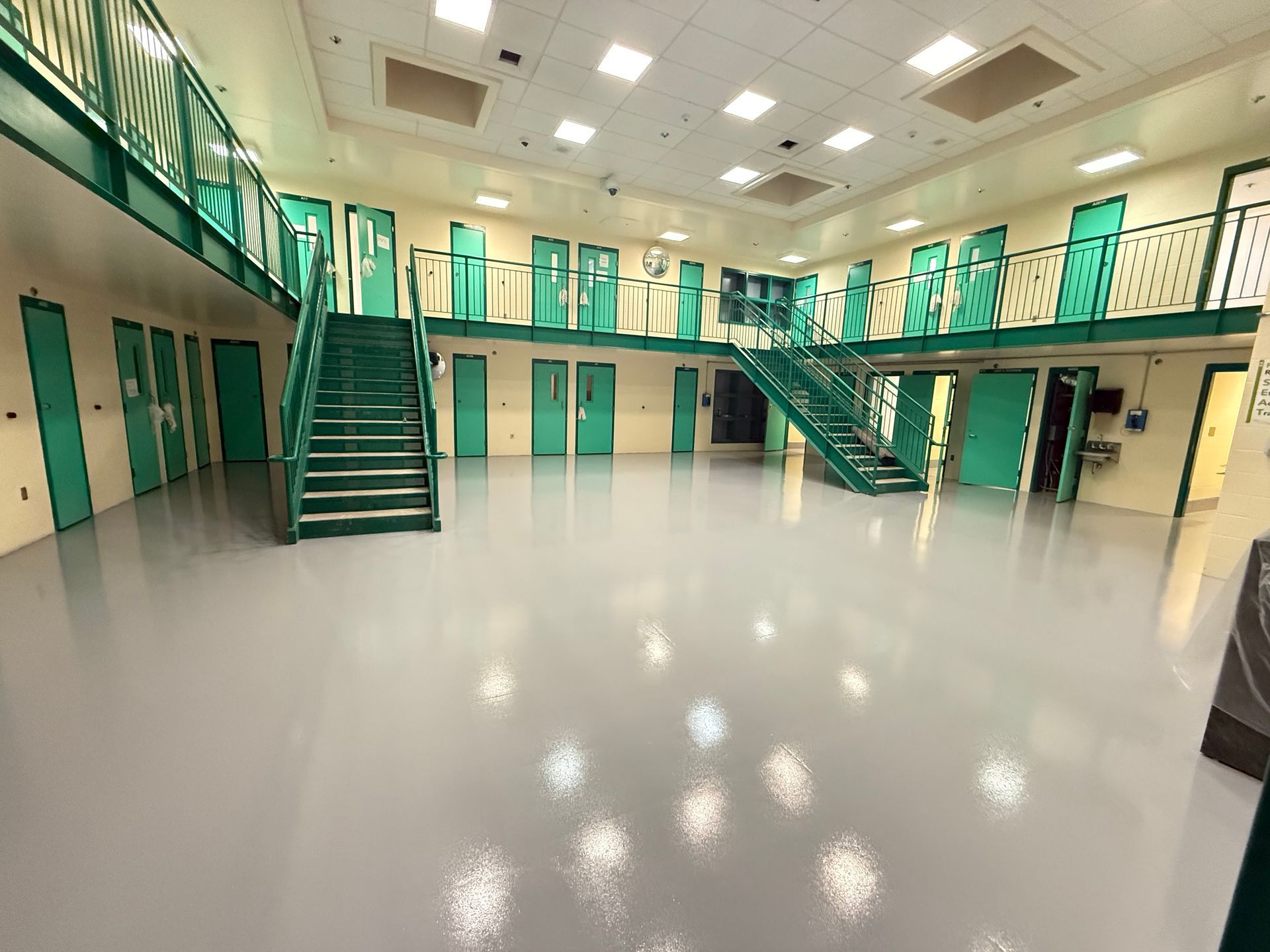 Elite Surface Coatings - Interior of a jail with two floors of green doors and walkways, gray floor, and green staircases.