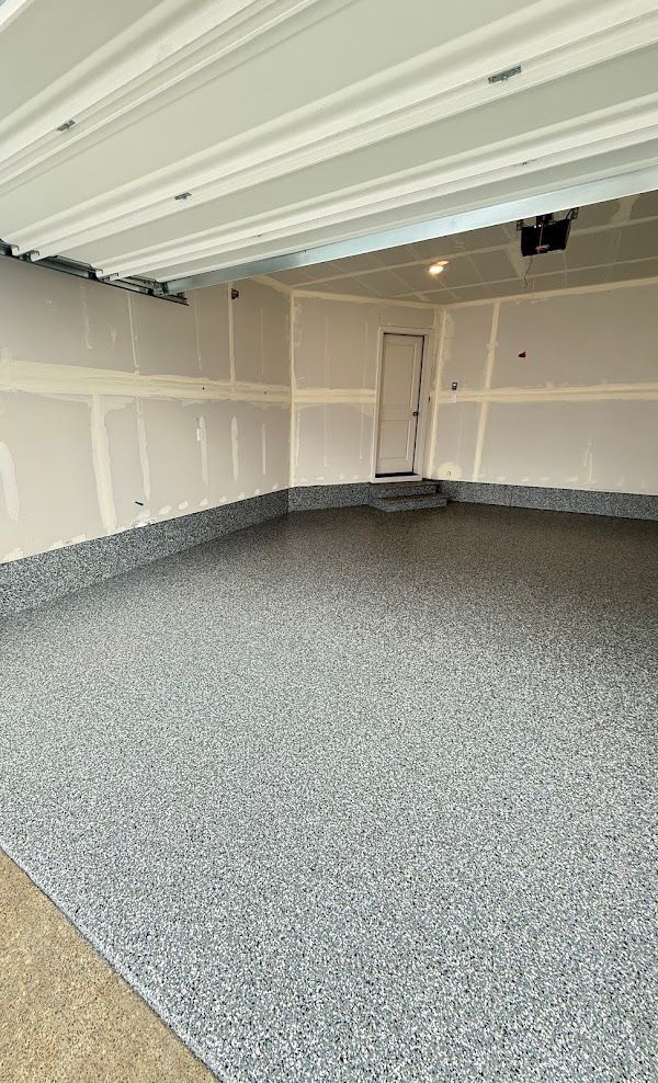 Elite Surface Coatings - Empty garage with a speckled gray floor, white walls, and a door.