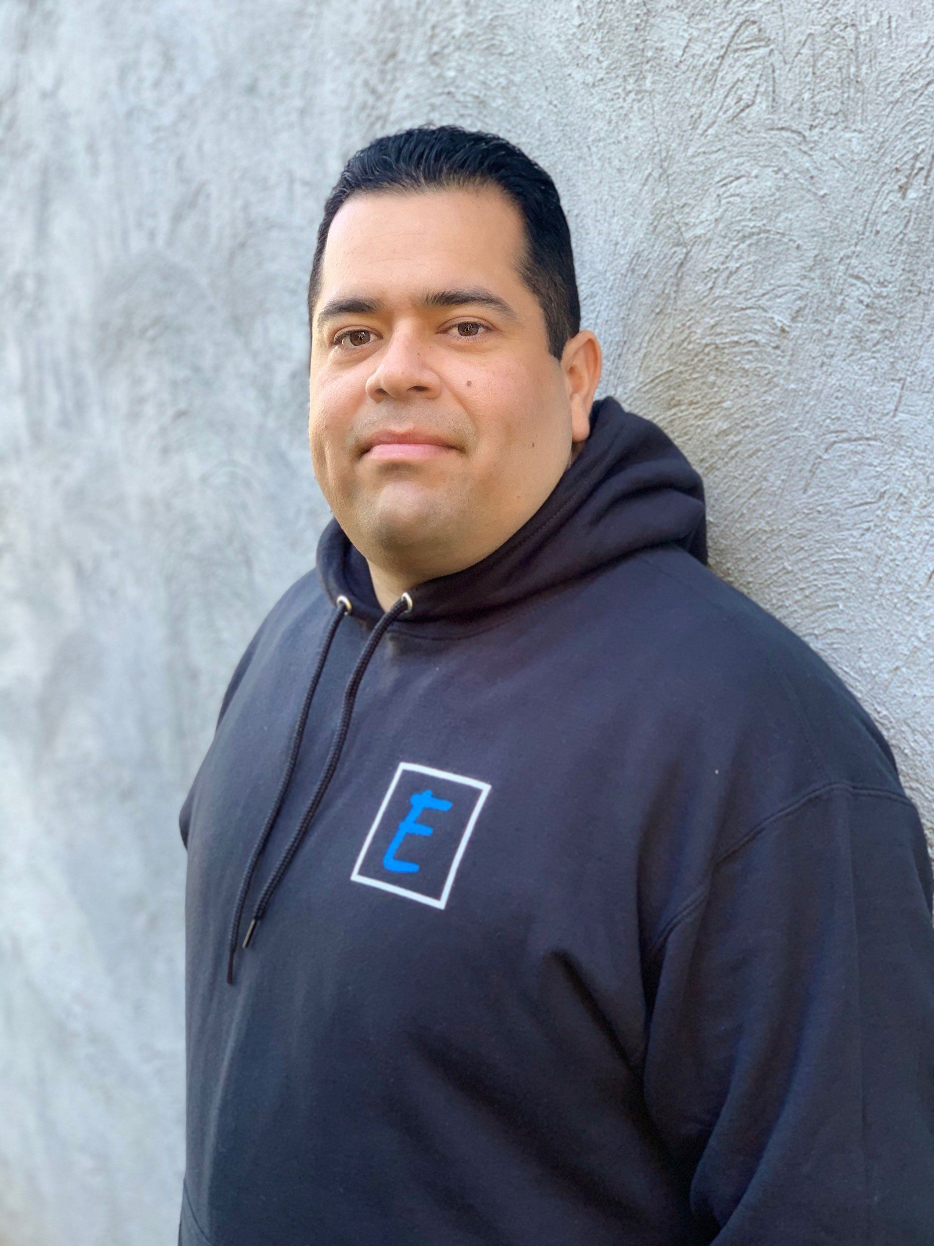 Elite Surface Coatings - A man in a blue hoodie is leaning against a wall and smiling.