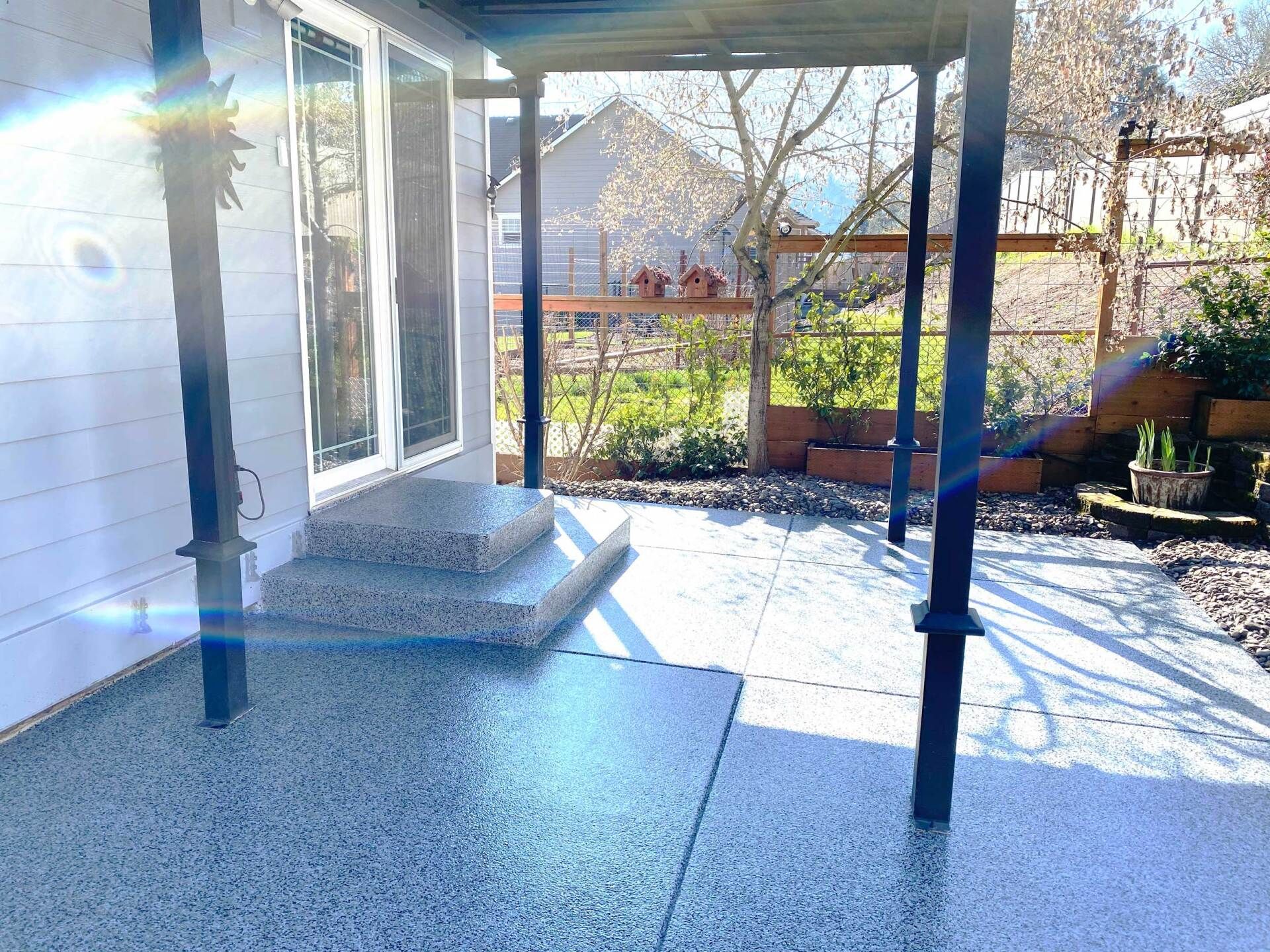 Elite Surface Coatings - Concrete patio with steps, black posts, and a glimpse of a backyard with a fence and greenery.