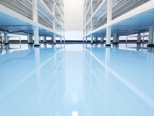 Elite Surface Coatings - Blue epoxy floor reflecting white columns and shelves in a warehouse.