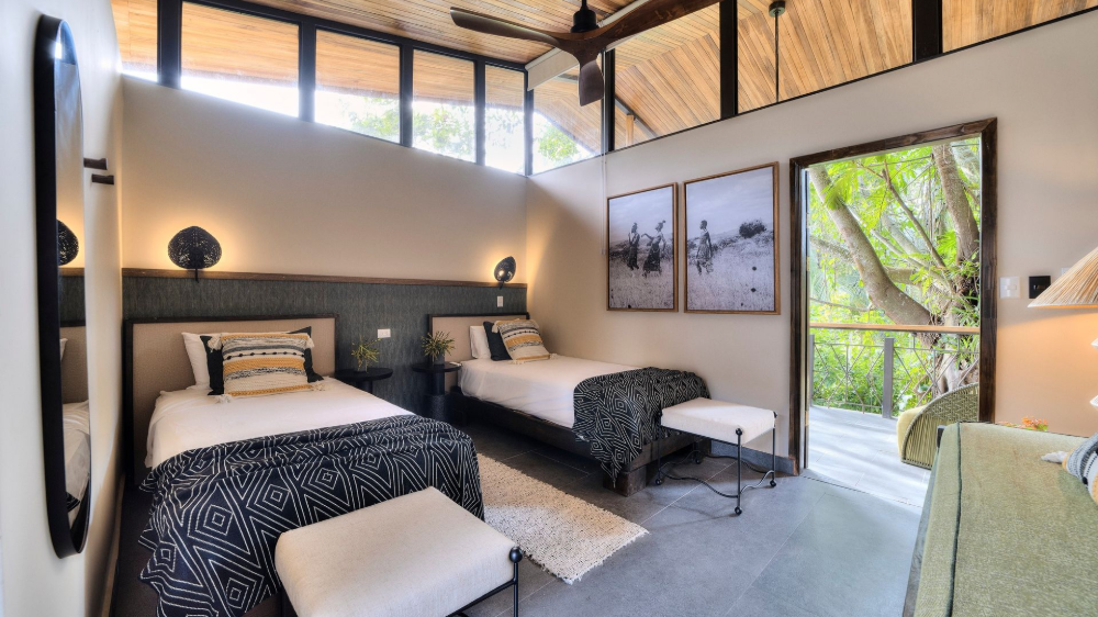 Bedroom with two twin beds, neutral tones, large window, and open doorway to a deck.