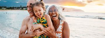Grandparents and child laughing on a beach at sunset.